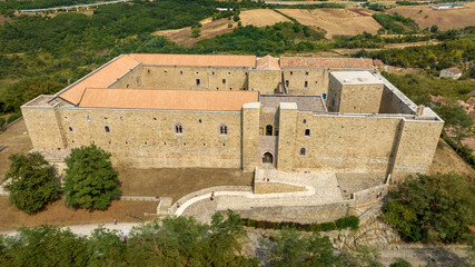 Aerial view of the entrance to Lagopesole Castle, located in Basilicata, Italy. It is a medieval castle dating back to the time of Frederick II. The fort sits atop a hill overlooking a vast landscape.