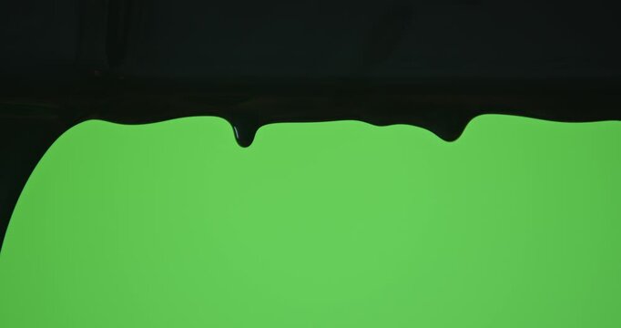 Close up of black paint flowing down a pane of glass against a green background, creating a minimalist abstract texture for design and advertising uses.