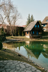 Obraz premium Small wooden rural house with ducks near pond reflection in Stanisici Ethno Village Bijeljina Bosnia and Herzegovina. Concept of countryside architecture cultural tourism and travel destination.