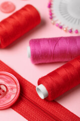 Composition with thread spools and zipper on pink background, closeup