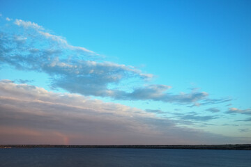 Obraz premium Tranquil blue sky with layered clouds over calm sea horizon at dusk, scenic coastal nature background with pastel light and wide copy space