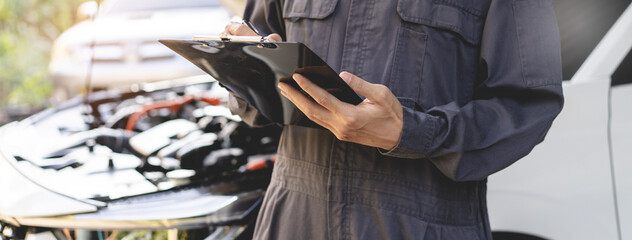 Obraz premium Auto check up and car service shop concept. Mechanic writing job checklist to clipboard to estimate repair quotation to client at workshop garage.