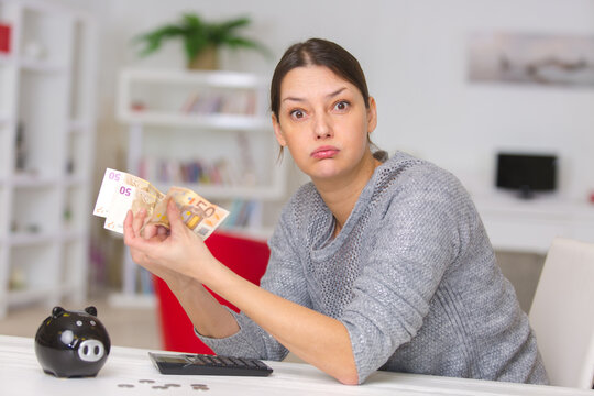 woman holding banknotes from piggybank and sighing with frustration