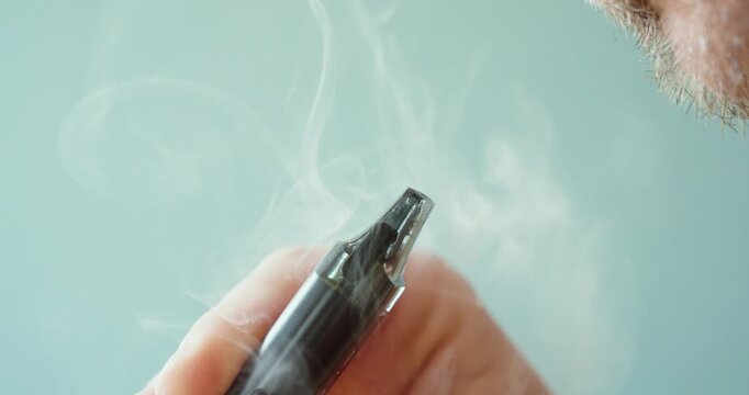 Close-up of a man exhaling vapor while using an electronic cigarette. Concept of vaping, nicotine alternatives, modern smoking habits, and e-cigarette lifestyle.