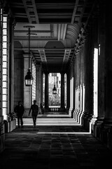 Naklejka premium Two people walk through a corridor at Greenwich University. The sunlight creates shadows on the ground and walls. The architecture shows the design of the space.