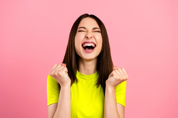 Excited young woman celebrating a victory with clenched fists and joyful laugh against a pink...
