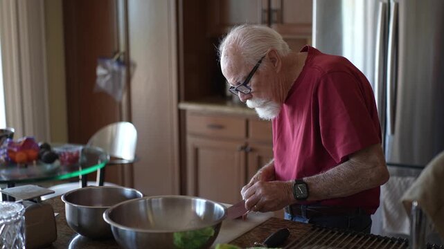 Senior man trims fat and cuts meat in a home kitchen while preparing ingredients for cooking a meal and organizing his workspace.