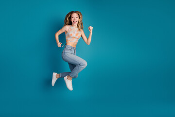 Happy young woman jumping in stylish casual outfit against blue background