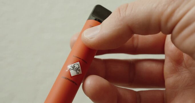 Close-up of a vape device showing a toxic hazard pictogram. Concept of nicotine warning, chemical risk, vaping dangers, and health awareness related to e-cigarettes.