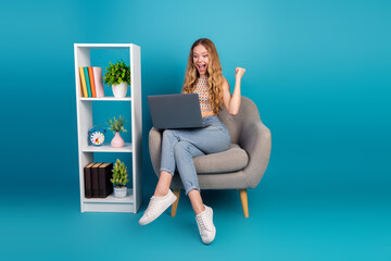 Young woman with laptop sits in a modern cozy setup smiling in a bright blue studio background