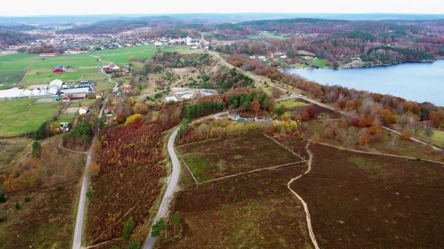 Aerial drone view of Fjaras Bracka landscape in Sweden showing nature centre, winding paths, autumn forest, open fields and nearby lake in scenic natural environment