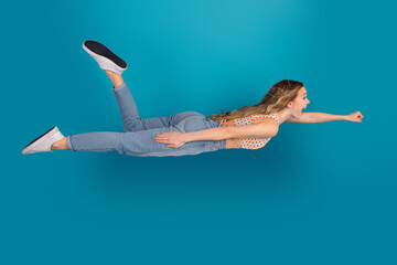 Fototapeta premium Energetic young woman jumps mid air in denim jeans and a striped top against a vivid blue backdrop