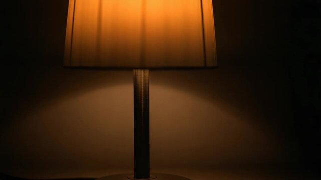 Moving camera upward revealing table lamp on table by plain wall, showing shade, shaft, power cord