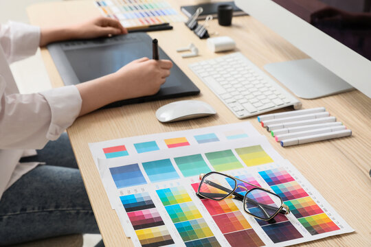 Female designer working with graphic tablet and color palettes at table in office, closeup