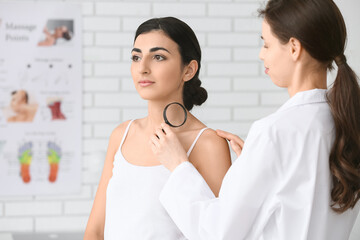 Dermatologist with magnifying glass examining moles of young woman in clinic