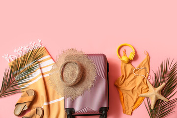 Fototapeta premium Composition with suitcase, swimsuit, tropical leaves and beach accessories on pink background