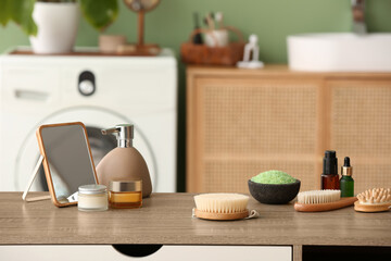 Different cosmetic products, mirror and massage brushes on wooden table in bathroom