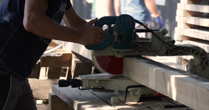 A workers cuts square timber with an electric saw.