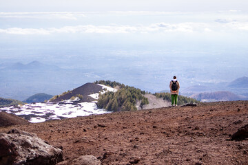 Small human figure standing on the edge of a volcanic crater at Mount Etna, Sicily. Contrast of black lava and snow creates a minimalist landscape with large copy space and strong scale of nature.  © Ina