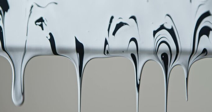 Close up of black and white paint flowing down a pane of glass against a soft grey background, creating a minimalist abstract texture for design and advertising uses.