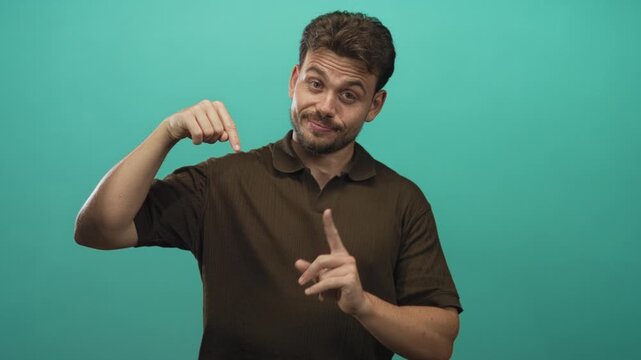 Man pointing finger to open palm while smiling in teal studio, presenting empty product space for caption or overlay; confident invitation.