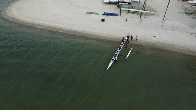 Angra Dos Reis, Brazil, January 13, 2025: People on shore on a tropical beach with white sand are preparing an outrigger canoe for a trip in the turquoise waters