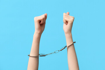 Female hands in handcuffs on blue background