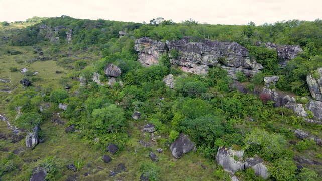 Aerial view showcasing rocky cliffs surrounded by dense green foliage under a cloudy sky in San Jos&eacute; del Guaviare, Colombia.