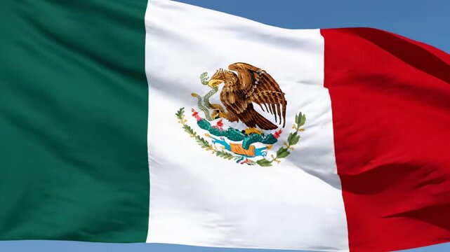 Close-up of the vibrant Mexican flag waving proudly against a clear blue sky, showcasing its iconic eagle and snake emblem.
