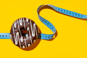 Blue measuring tape, sweet chocolate donut on yellow background with sun shadows, flat lay....