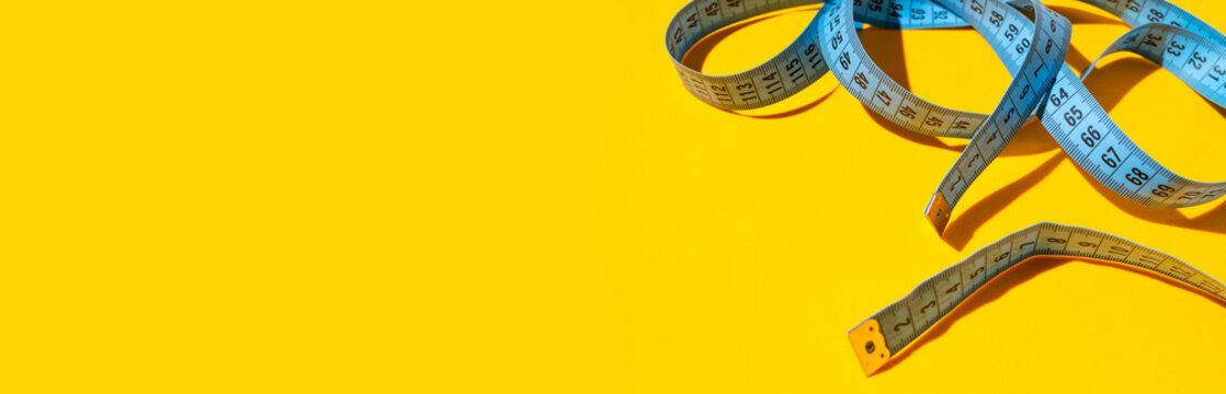 Blue measuring tape, centimeter on yellow background with sun shadow. Tape for tracking body measurements, sewing clothes. Minimalist concept for diet, weight loss, fitness. Flat lay top view