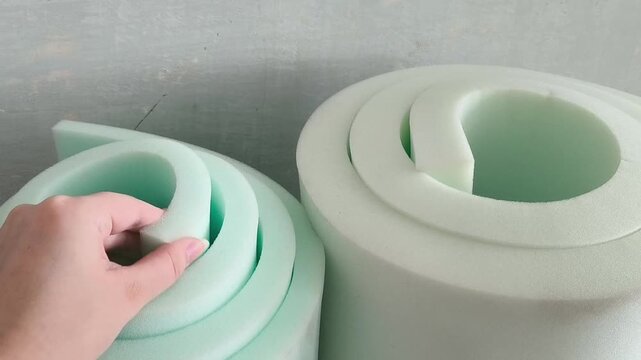 A hand touches the soft foam in a roll in close-up. Thickness of the foam roll. Wall insulation, sound insulation, repair
