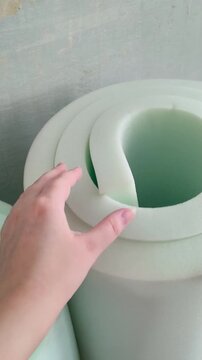 A hand touches the soft foam in a roll in close-up. Thickness of the foam roll. Wall insulation, sound insulation, repair