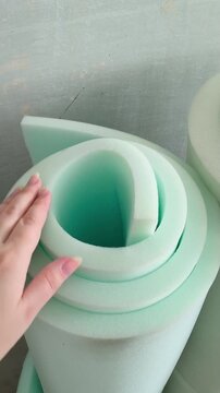A hand touches the soft foam in a roll in close-up. Thickness of the foam roll. Wall insulation, sound insulation, repair