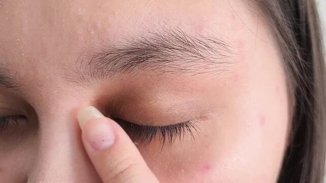 A woman touches natural black thick eyelashes with her finger.