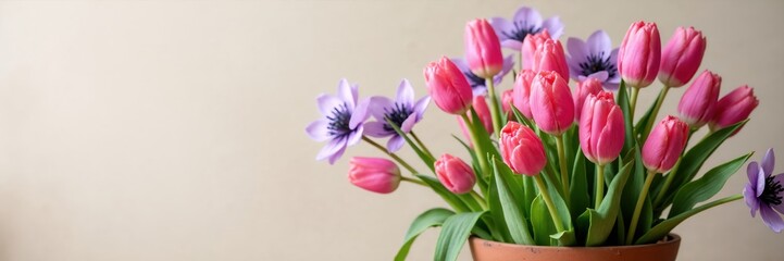 Naklejka premium Pink tulips and purple anemones in a rustic terracotta pot. Fresh spring floral bouquet arrangement against a neutral beige background. Copy space for text