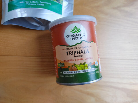 Close up of Organic India Triphala powder jar on a light wooden background