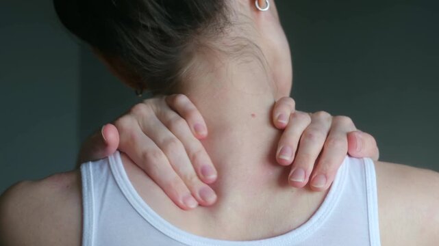 Woman in white tank top massaging her tired neck and tense shoulders, trying to relieve muscle stiffness, pain caused by overwork, stress, sedentary lifestyle. Woman massaging neck pain her shoulders