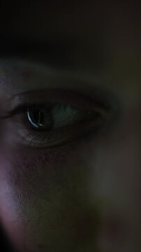Vertical screen close up human eye in darkness with intense focus reflecting hidden content representing secrecy curiosity risky online behavior privacy concerns and forbidden digital experience