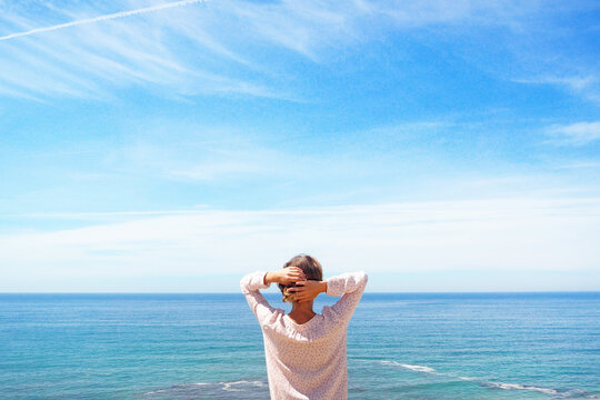 Rear view of a woman standing by the sea with her hands behind her head, Sesimbra, Lisbon, Portugal