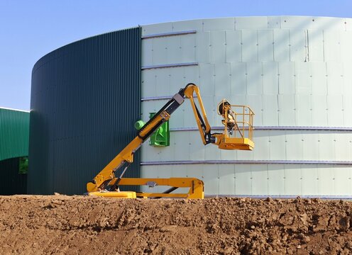 Yellow cherry picker working on the construction of a large industrial tank in the oil industry.
