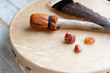 Meditation drum and paddle with sacred feather and carnelian crystals on an white washed table top. 