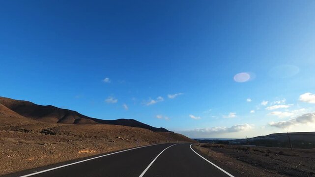 POV driving along empty countryside asphalt road in sunny desert environment with distant mountains and clear blue sky. Freedom exploration concept symbolizing adventure lifestyle and independent disc
