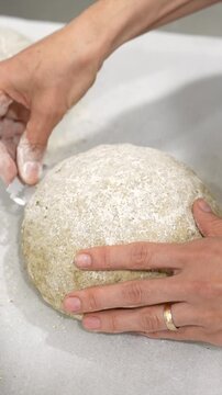 Baker's hands carefully scoring a raw sourdough loaf with a lame blade before baking, preparing the dough for the oven to ensure a beautiful crust and proper expansion of the bread