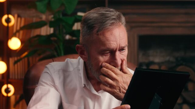 Caucasian senior retired old business man looking at photo in frame holding framed picture suffering lonely nostalgy elder businessman male professional missing family children grandchildren at office