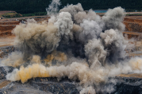 Explosive activity in large open pit gold mine with dust and smoke rising