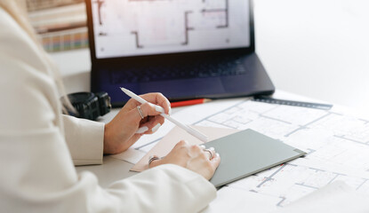 Female architect reviewing floor plans on tablet in modern office. Interior designer choosing materials and color for decorations.