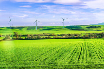 green sunset field with grass hills and wind power plant generating pure clean electric enerdy on background of landscape. green energy of future from wind turbines