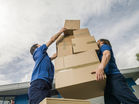 Two men carrying overloaded tower of boxes