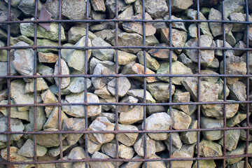 Gabion wall background with natural grey stones contained behind a rusty iron wire mesh grid.
